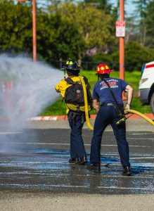 Two firefighters actively extinguishing a fire with a powerful water hose on a city street.