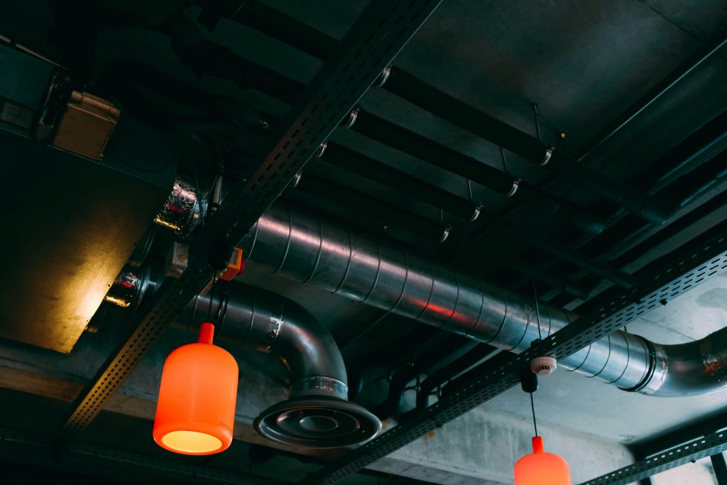 Low-angle view of a modern industrial ceiling featuring ducts and red lamps.